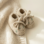 Beige hand-knitted newborn booties with green floral embroidery, part of a premium knit newborn clothes set in Egyptian cotton