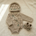 Handmade newborn knit romper with custom embroidery displayed in a cozy lifestyle setting. Premium Egyptian cotton knit newborn clothes including a matching bonnet and booties.