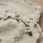 Close-up of luxurious handmade knit newborn clothes, featuring delicate floral embroidery on a soft cotton fabric – the perfect newborn gift.
